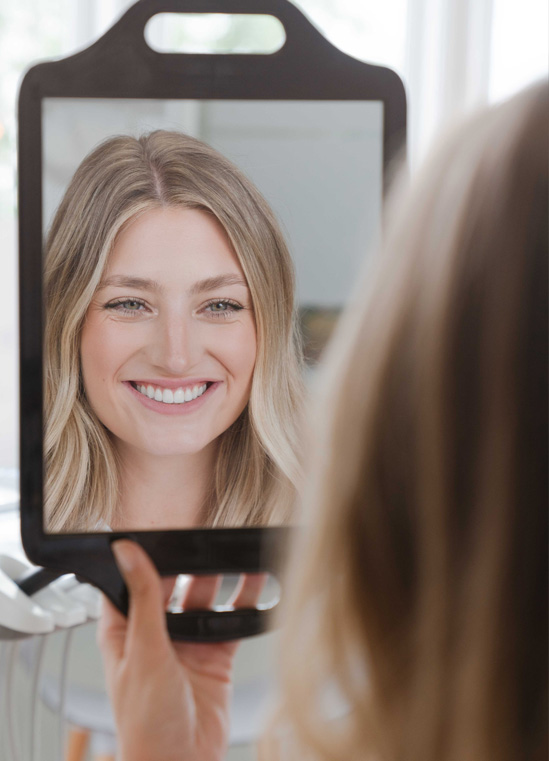 Patient smiling at her teeth in a hand mirror at Bespoke Dental